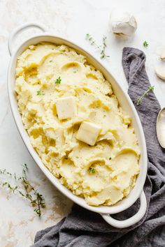 mashed potatoes with butter and parsley in a white casserole dish on a gray towel