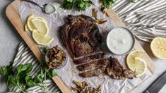 the steak is sliced and ready to be served with sauces, lemon wedges and parsley