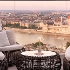 two wicker chairs and a coffee table on top of a balcony overlooking a city