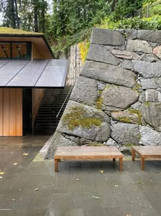 two wooden benches sitting in front of a stone wall and steps leading up to a building