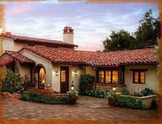 an adobe style house with red tile roofing and brick walkway leading to the front door