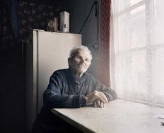 an old man sitting at a table in front of a window