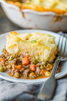 a white plate topped with mashed potatoes covered in meat and veggies next to a fork