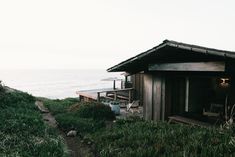 a small wooden cabin sitting on top of a lush green hillside next to the ocean