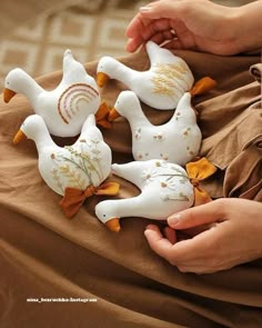 four white birds with yellow flowers on them sitting on a brown blanket, one being held by a woman's hand