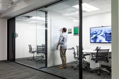 a man standing in an office looking at a large screen on the wall behind him