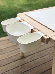 three white bowls sitting on top of a wooden table next to a green grass field