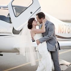 a bride and groom kissing in front of an airplane