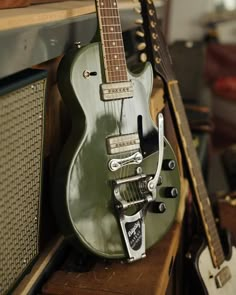 an old green guitar sitting on top of a wooden shelf next to other musical instruments