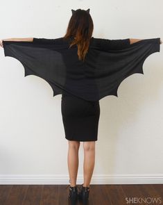 a woman wearing a bat costume standing in front of a white wall with her arms outstretched