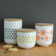 three ceramic containers with designs on them sitting on a wooden table next to crackers