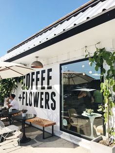 a man sitting at a table in front of a coffee and flowers sign on the side of a building