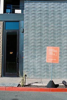 an orange sign sitting on the side of a road next to a tall gray building