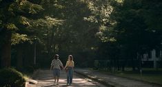 two people walking down a path in the middle of a park with trees on both sides