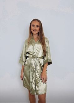 a woman standing in front of a white wall wearing a gold robe and smiling at the camera