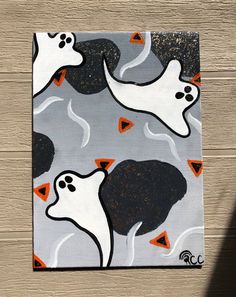 a painting on a wooden surface with white ghost faces and orange triangle shapes in the background