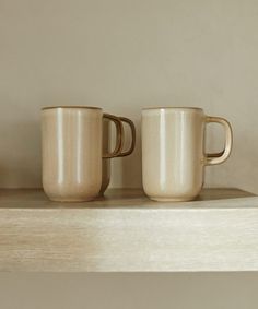 two coffee mugs sitting on top of a shelf