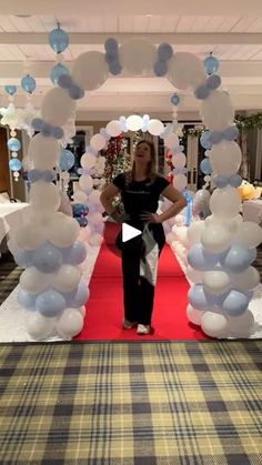 a woman standing in front of a red carpeted floor with white and blue balloons