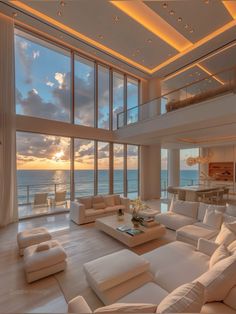 a living room filled with lots of white furniture and large windows overlooking the ocean at sunset