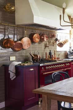 a kitchen with red cabinets and copper pans hanging on the wall above an oven