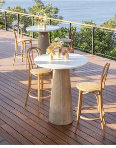 an outdoor table and chairs on a wooden deck overlooking the ocean with flowers in vases