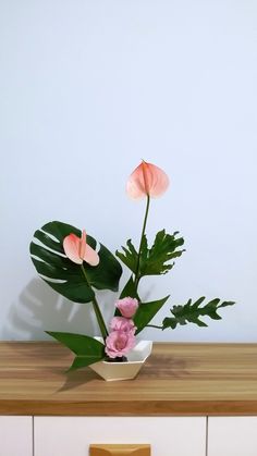 a plant with pink flowers in a white vase on top of a wooden countertop