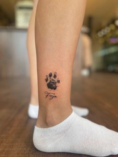 a person with a dog paw tattoo on their leg and foot, standing on a wooden floor