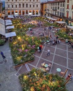 an aerial view of a city square with people sitting and walking around it at dusk