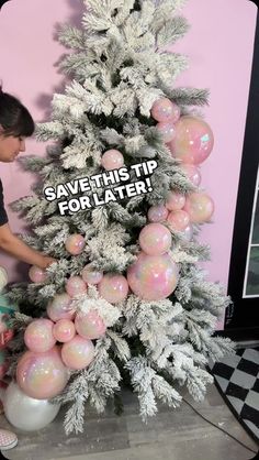 a woman decorating a white christmas tree with pink and silver ornaments on the top