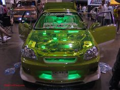 a green car with its hood up and lights on