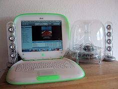 an open laptop computer sitting on top of a wooden desk next to speakers and a glass dome