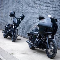 two motorcycles parked next to each other near a brick wall