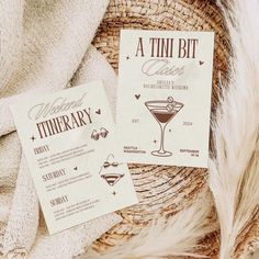 two cocktail menus sitting next to each other on top of a basket with feathers