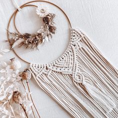 a white and gold dream catcher with feathers on it's side next to dried flowers