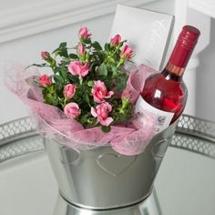 a bottle of wine and some pink flowers in a silver bucket on a glass table