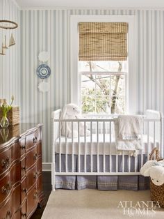 a baby's room with blue and white stripes on the walls, crib, dresser and window