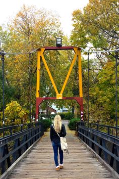 a woman walking across a bridge in the fall