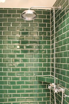 a green tiled shower stall with hand held shower head