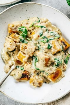 a white plate topped with pasta covered in cheese and spinach sauce next to a fork