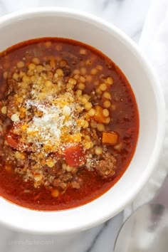 a white bowl filled with chili and corn on top of a marble counter next to a spoon