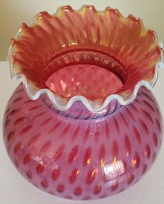 a pink glass vase sitting on top of a white table next to a red bowl