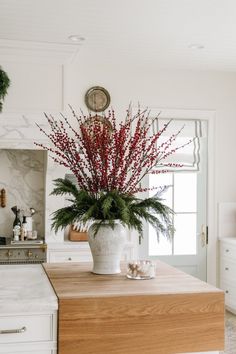 a vase filled with red flowers sitting on top of a wooden table in a kitchen