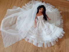 a doll is wearing a white dress with a veil on it's head and sitting on the floor