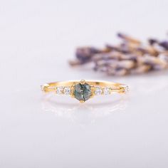 a gold ring with a green and white stone in the middle, surrounded by lavender flowers