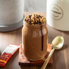 a jar filled with chocolate and nuts on top of a wooden table next to a spoon