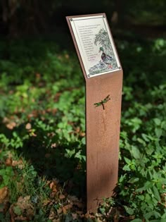 there is a plaque in the grass with a dragonfly on it and a tree behind it