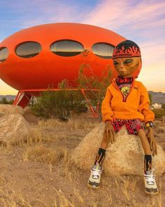 a doll sitting on top of a rock in front of an orange structure