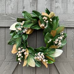 a wreath with white flowers and green leaves hanging on a wooden door frame in front of a wood paneled wall