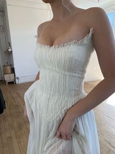 a woman in a white dress standing on a wooden floor with her hand on her hip