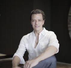 a man sitting on the floor in front of a wall with a clock behind him